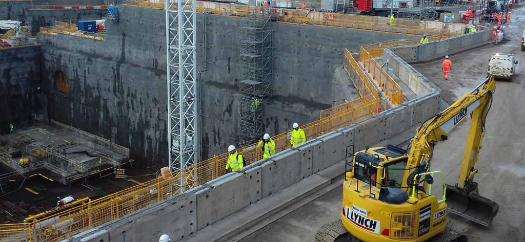Concrete barriers being installed at a nuclear plant construction site, with yellow digger nearby
